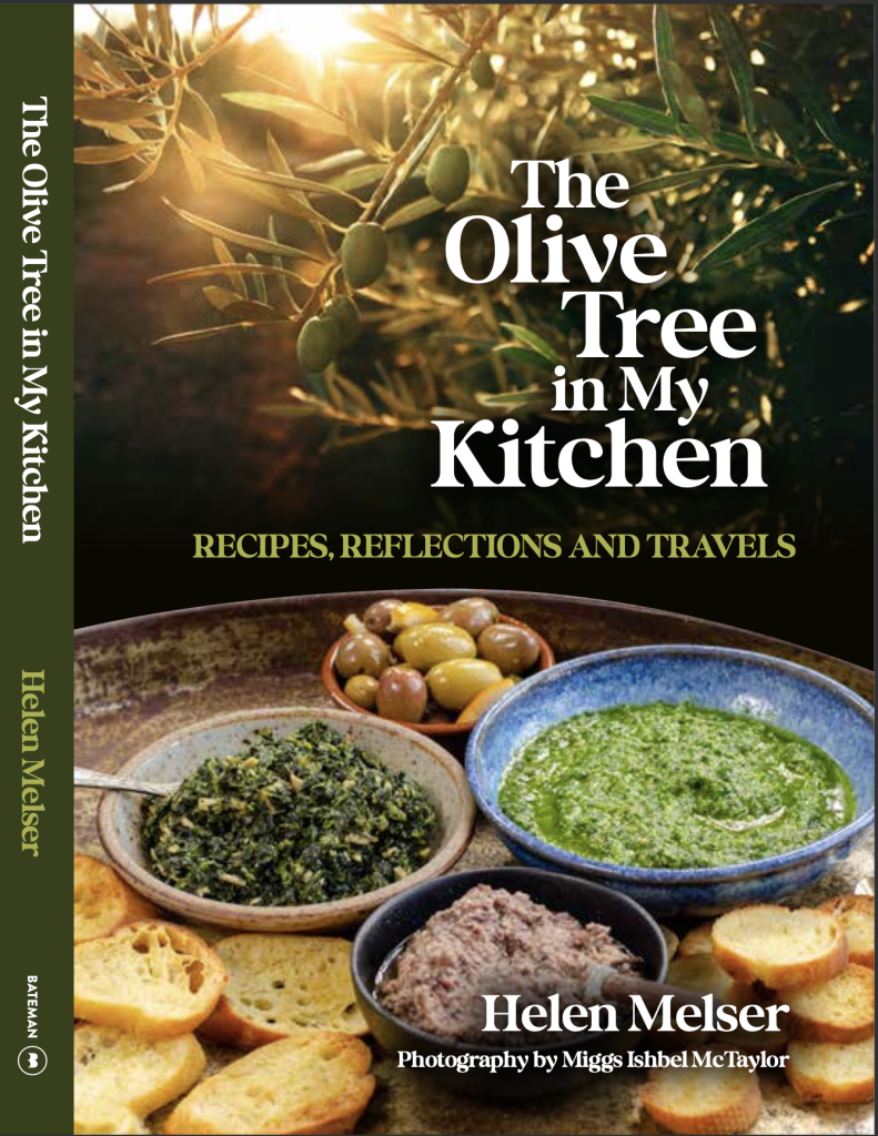 The front cover with spine showing of the cookbook 'The Olive Tree in my Kitchen" by Helen Melser showing a tray of food infant of an olive free with the sun in the background